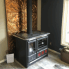 Fogão a Lenha em Ferro Fundido - Nordica Extraflame Rosa XXL com placa dourada atrás, em cozinha moderna.