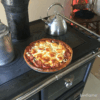 Vista superior do Fogão a Lenha em Ferro Fundido - Nordica Extraflame Rosa XXL com pizza assada, destacando o seu forno de alta capacidade.