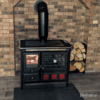 Fogão a Lenha em Ferro Fundido - Nordica Extraflame Rosa XXL em cozinha com paredes de tijolo à vista, criando um ambiente acolhedor e rústico.
